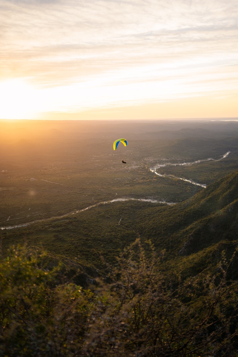 Paraglider soaring high above green terrain in sunset