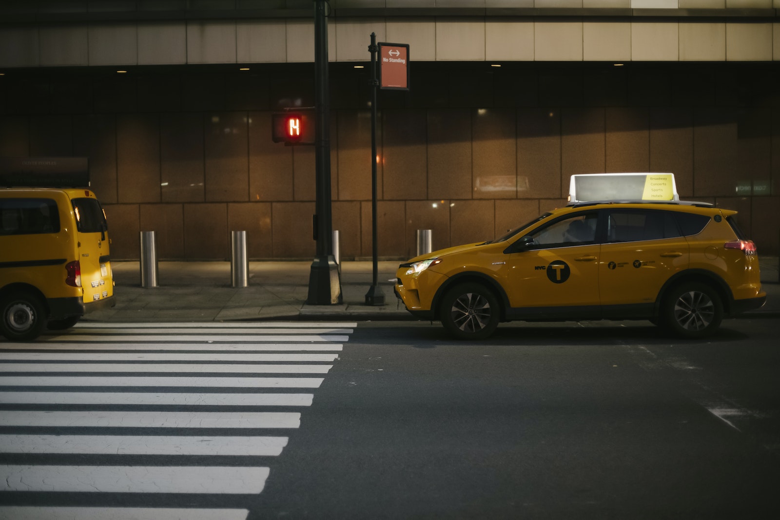 Modern shiny yellow SUV taxi car stopped near traffic light at zebra crossing in evening