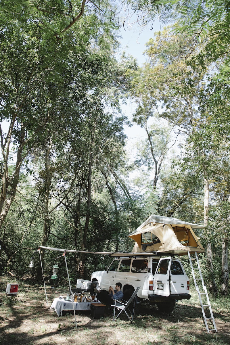 Camping car with tent on roof parked in forest in sunlight