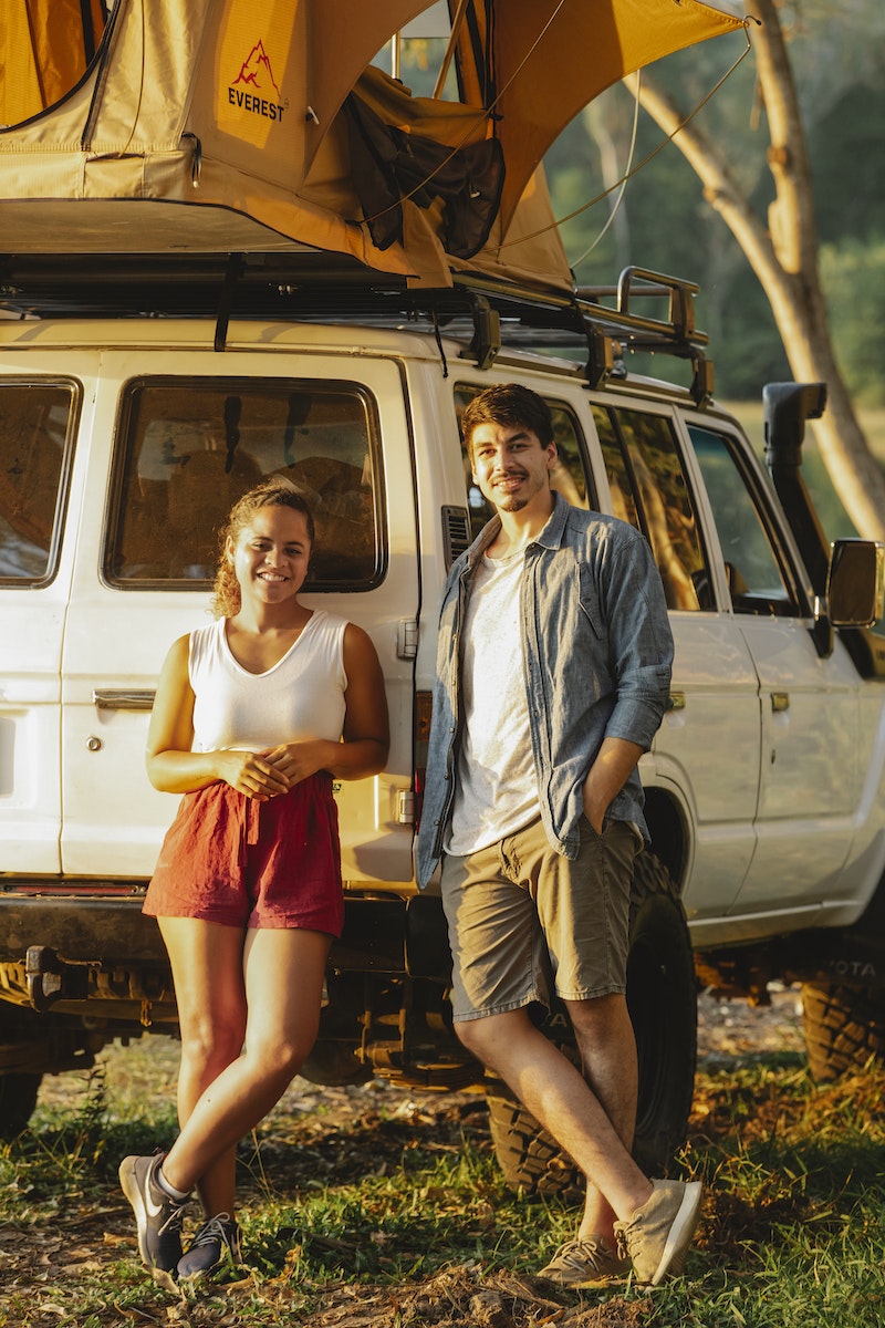 Cheerful diverse couple recreating near camping tent in green forest