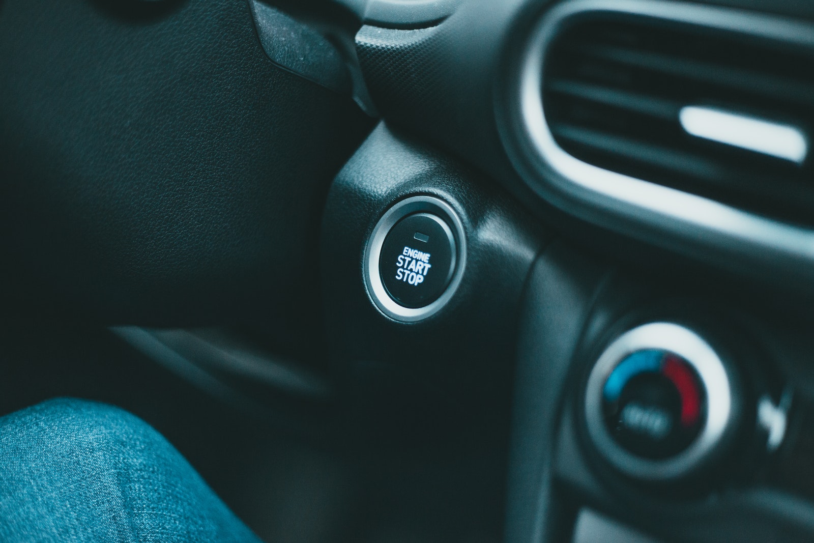 Closeup of black shiny dashboard with engine start button and conditioner controller of modern car in daylight