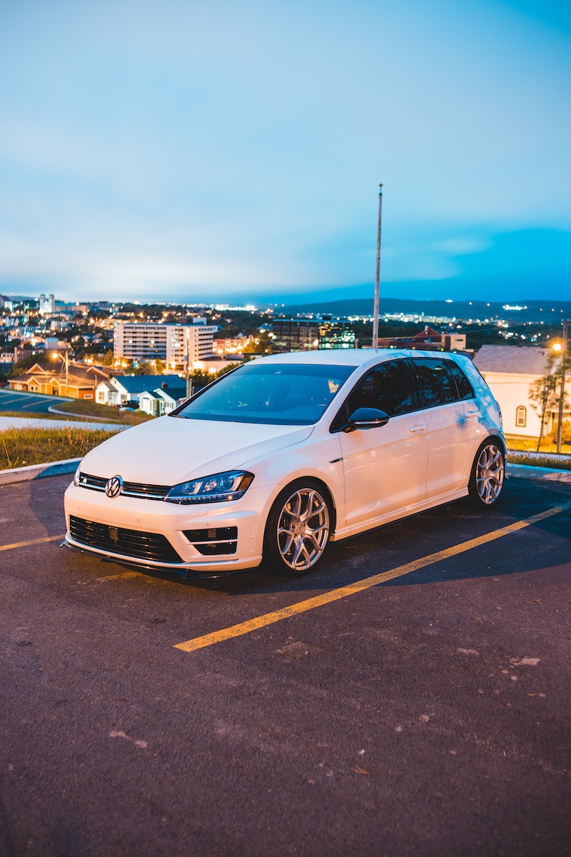 White compact vehicle on asphalt parking lot in modern night city with bright lights under blue sky