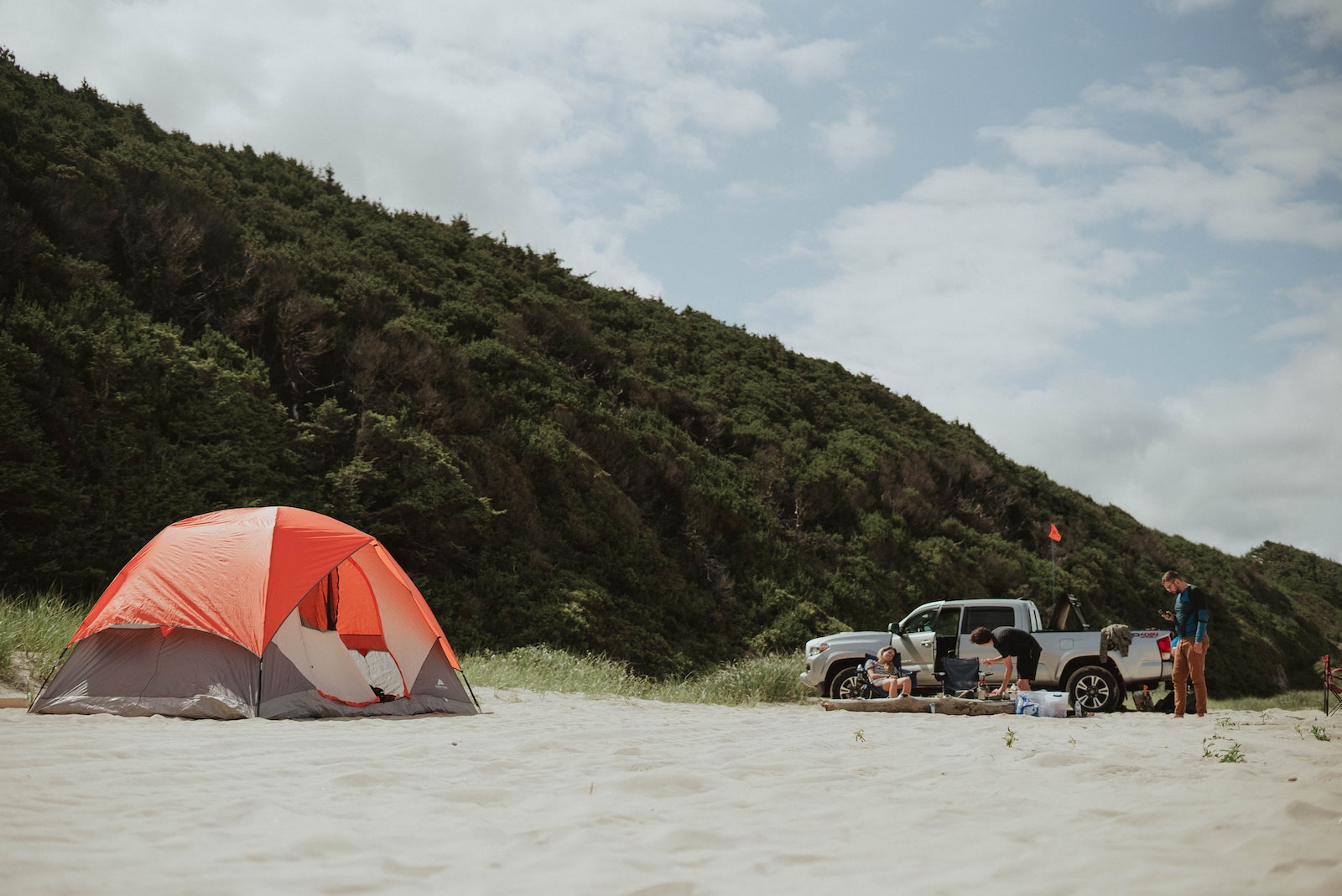 Travelers with car and tent on sandy beach having wild trip in valley with green hills