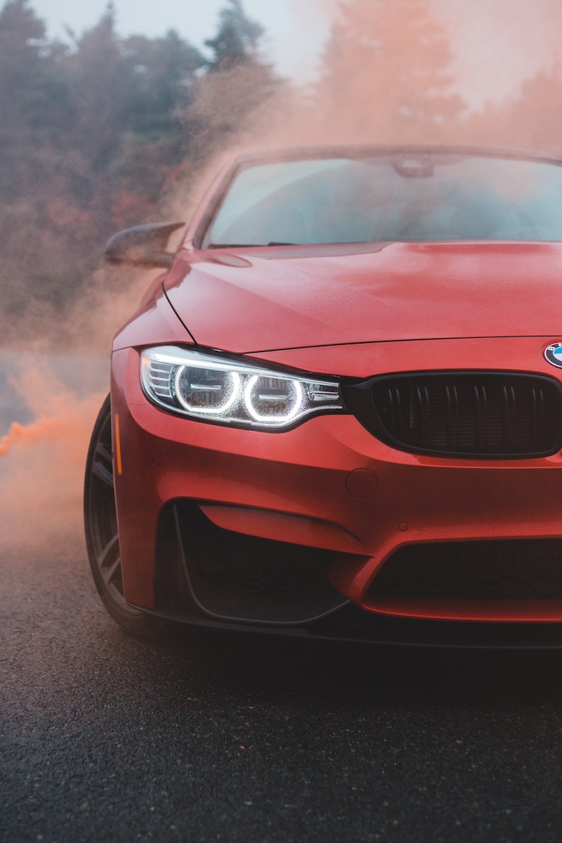 Red car with shiny headlights in colored smoke