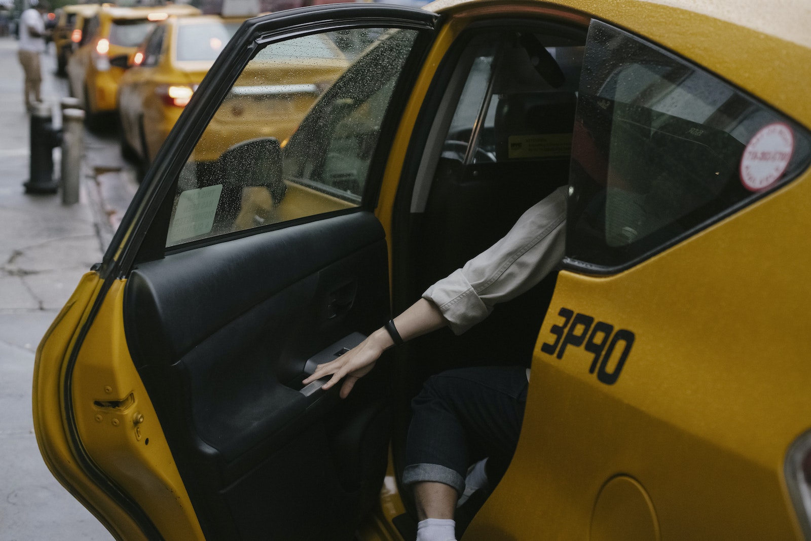 Anonymous passenger closing door of cab parked on roadside with blurred cars on background in rush hour on street in city