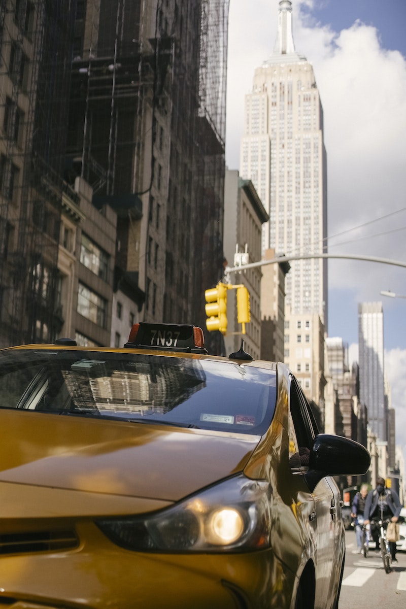 Contemporary cab automobile with glowing headlight on roadway near multistory buildings in New York City