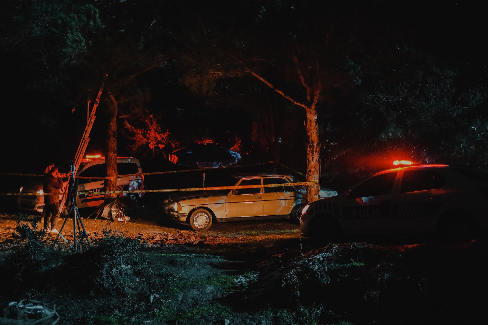 Investigators from police working on crime scene fenced with caution tape in woods at night